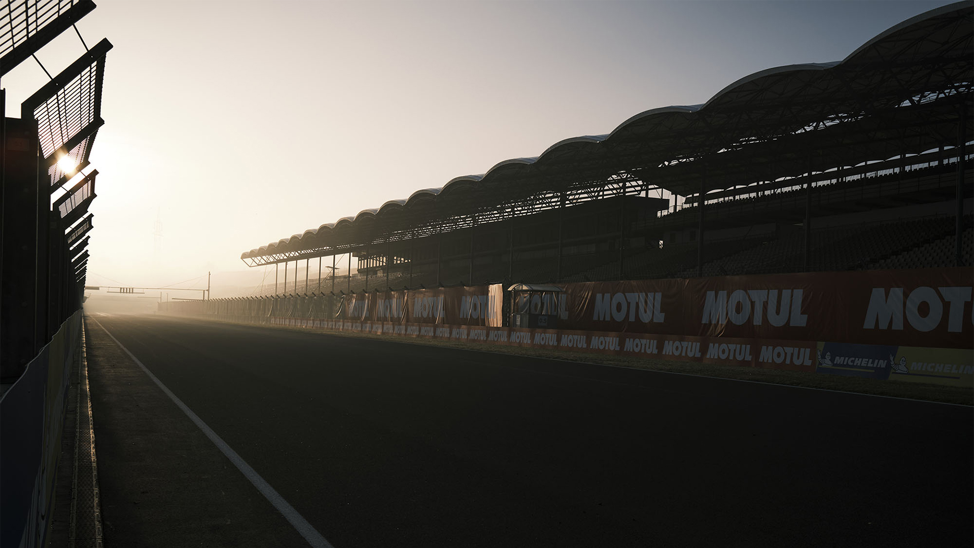 The empty main straight at sunrise, grandstands in silhouette.
